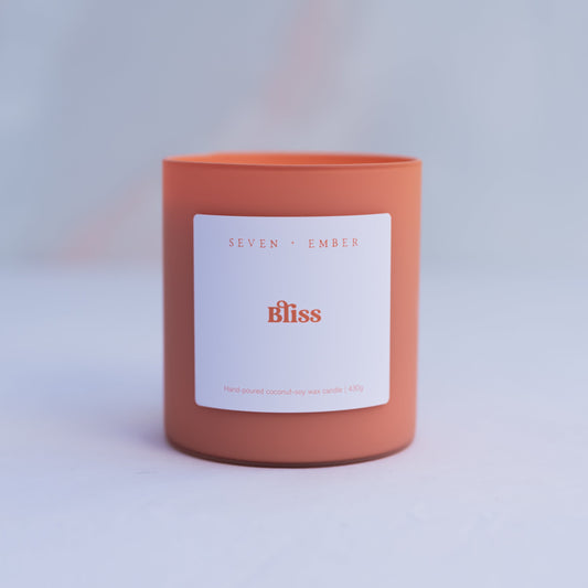 Bliss candle with a white label in a orange sorbet coloured frosted glass jar on a marble surface