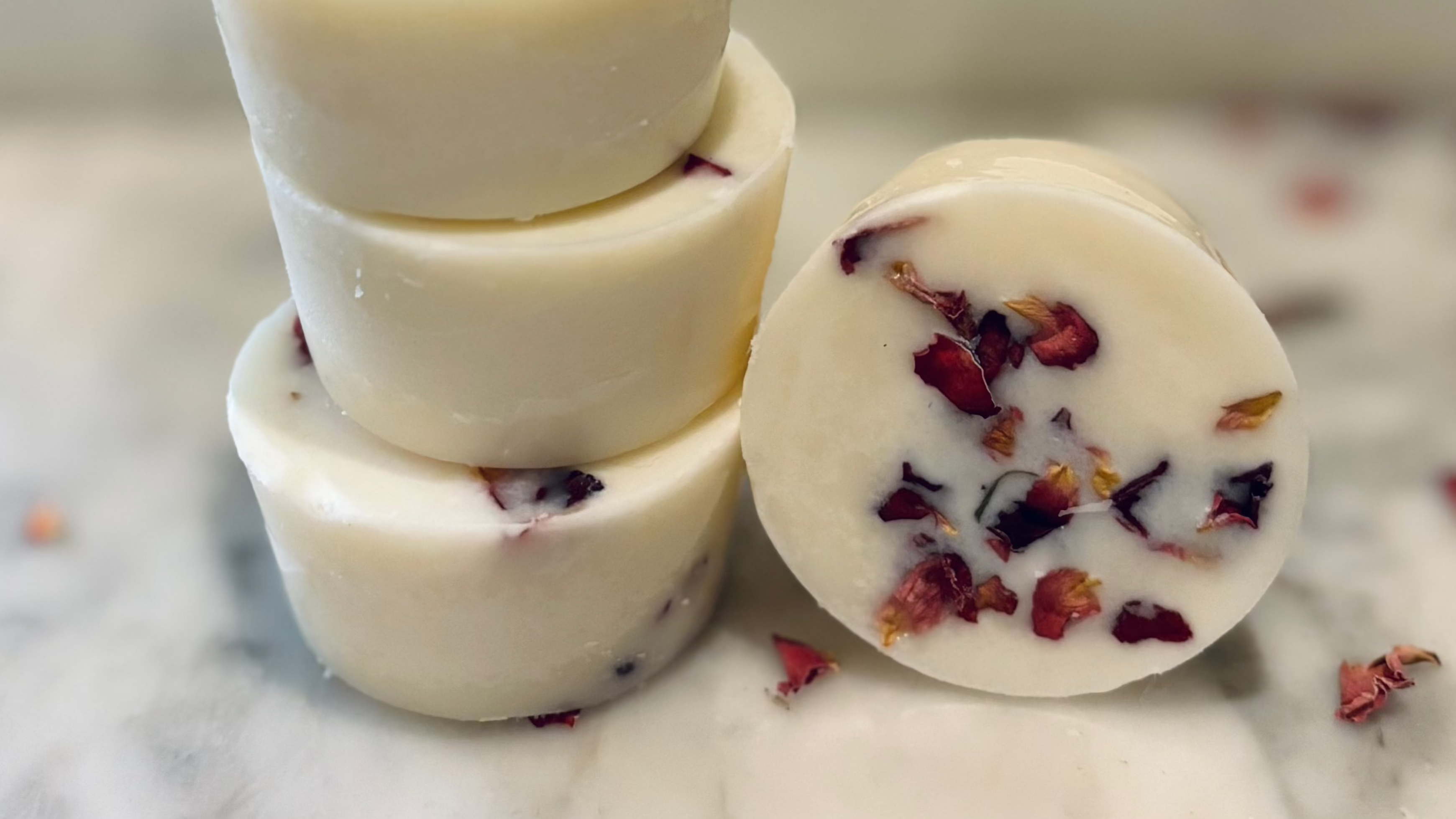 Stack of botanical wax melts with floral petals on a marble surface