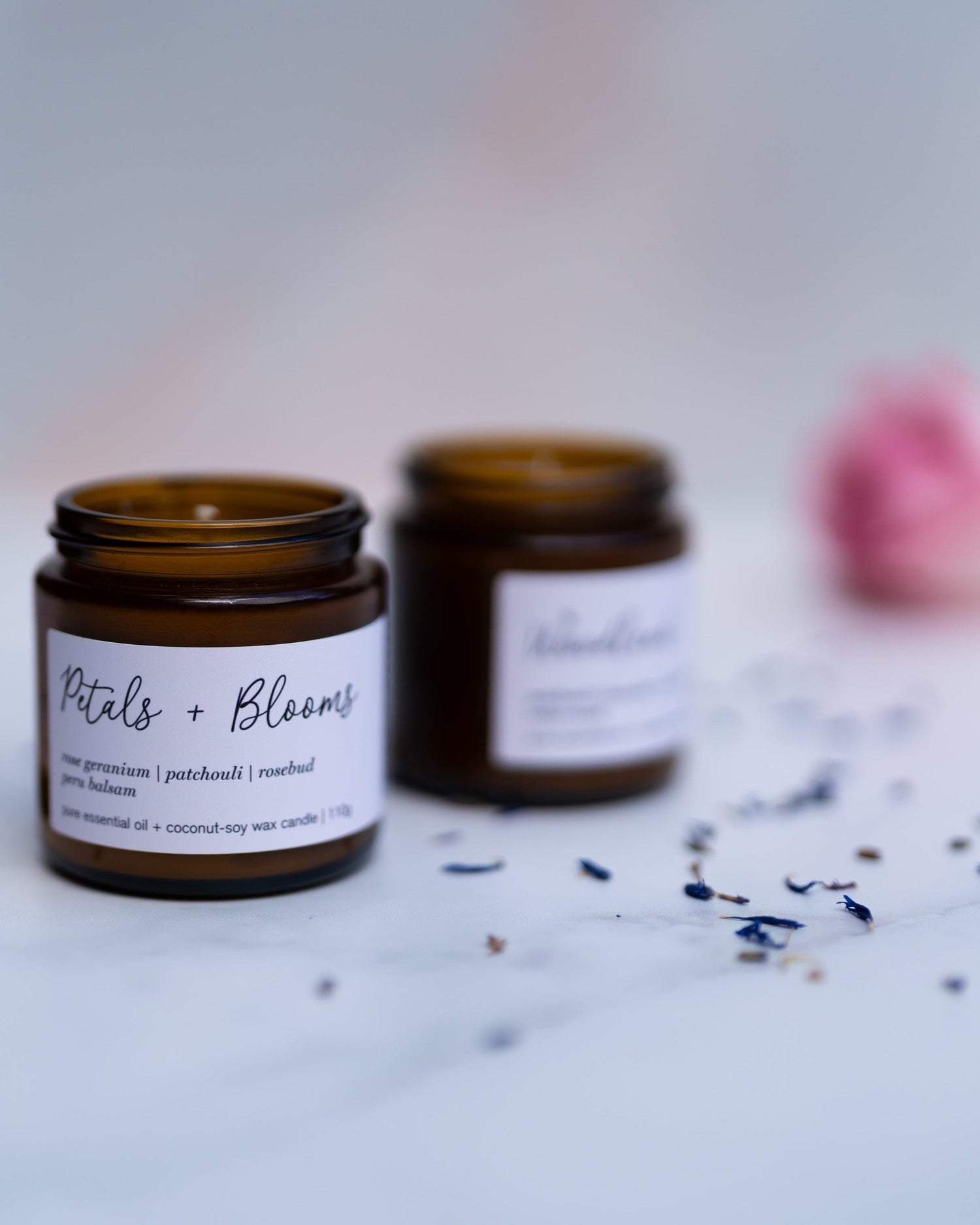 A Mini Petals in Bloom Candle and a Mini Woodland Candle on a marble background with lavender flowers and a pink rose