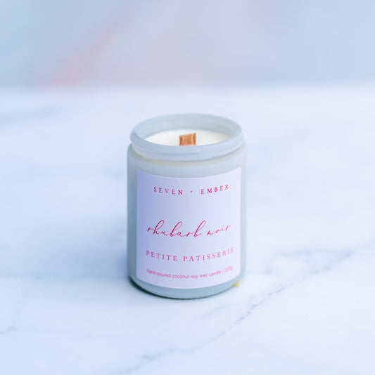 Rhubarb noir candle with a wooden wick in a white screw top jar on a marble surface