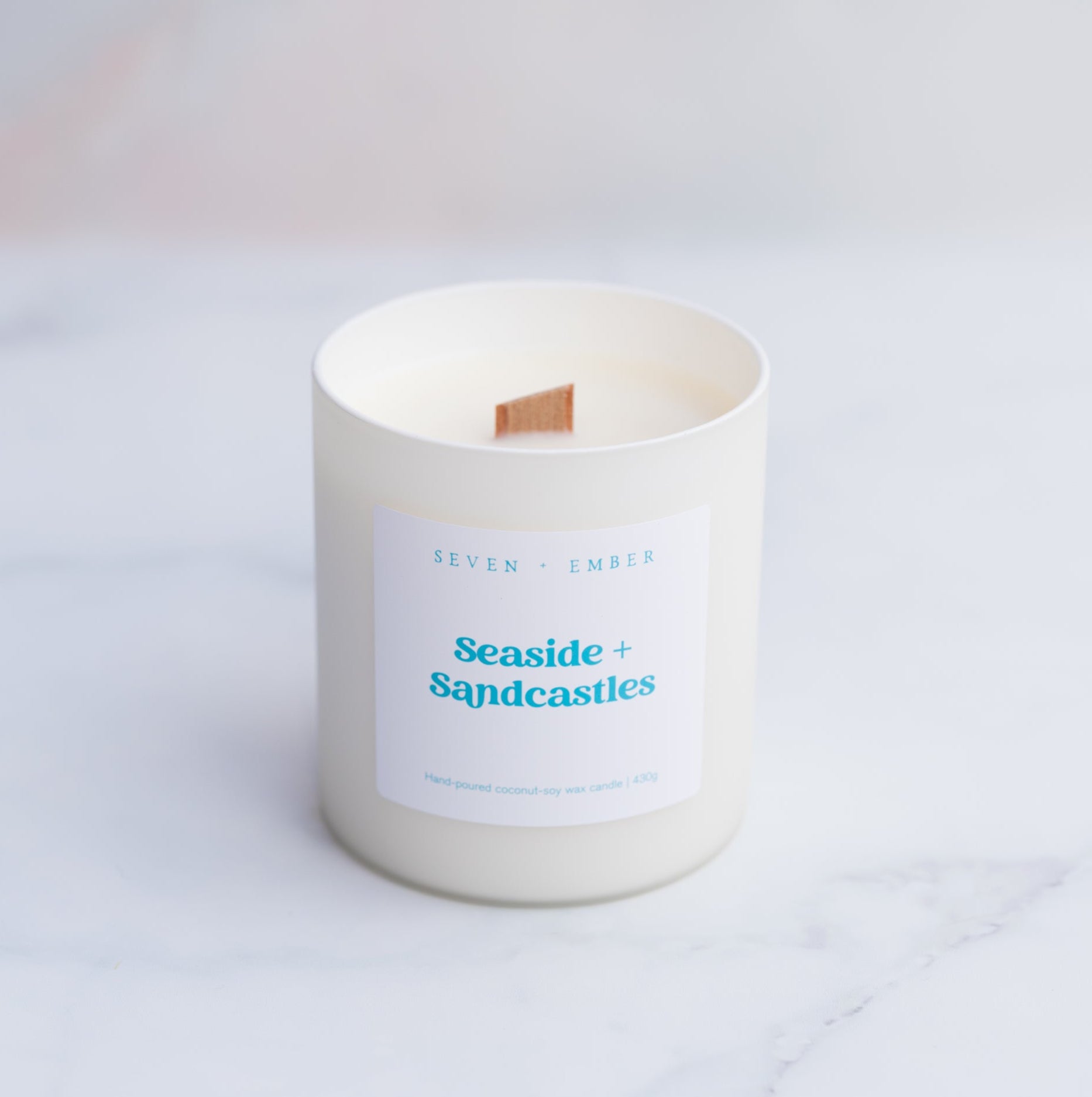 A seaside and sandcastles candle with a wooden wick in a creamy white frosted glass vessel
