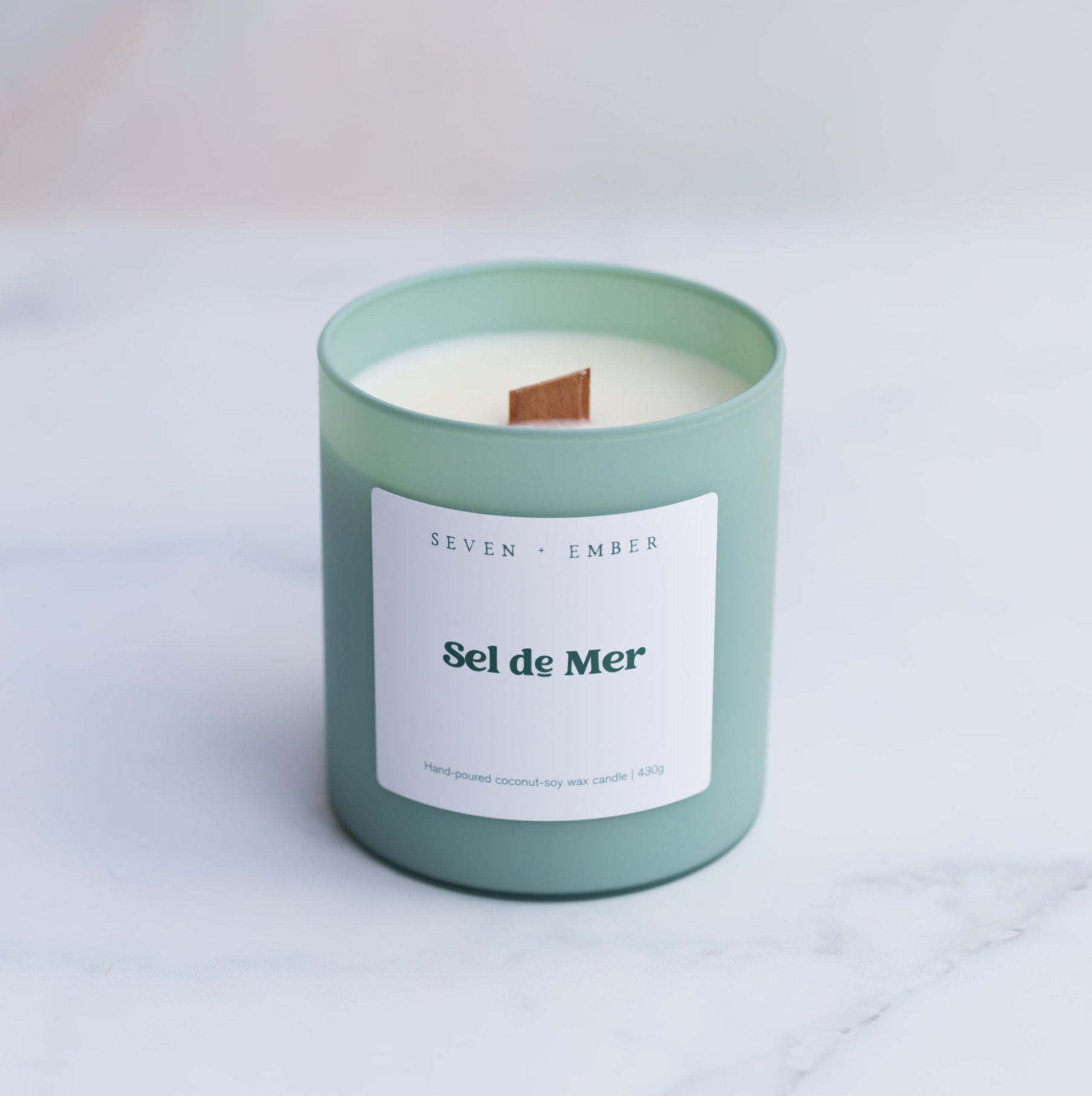 sel de mer scented candle with a wooden wick in a sage green frosted glass vessel on a marble background