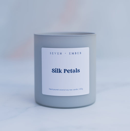 Silk petals candle in a light grey frosted vessel on a blurred marble background