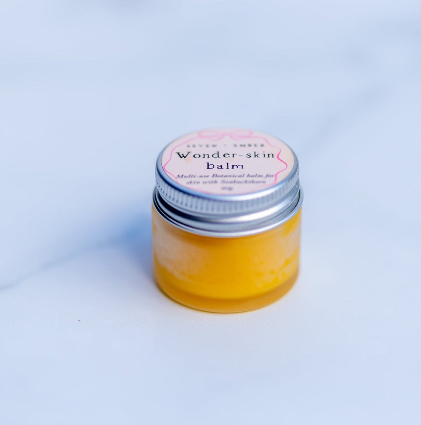 Wonder skin balm in a mini frosted jar with silver lip filled with sunshine yellow balm on a marble surface