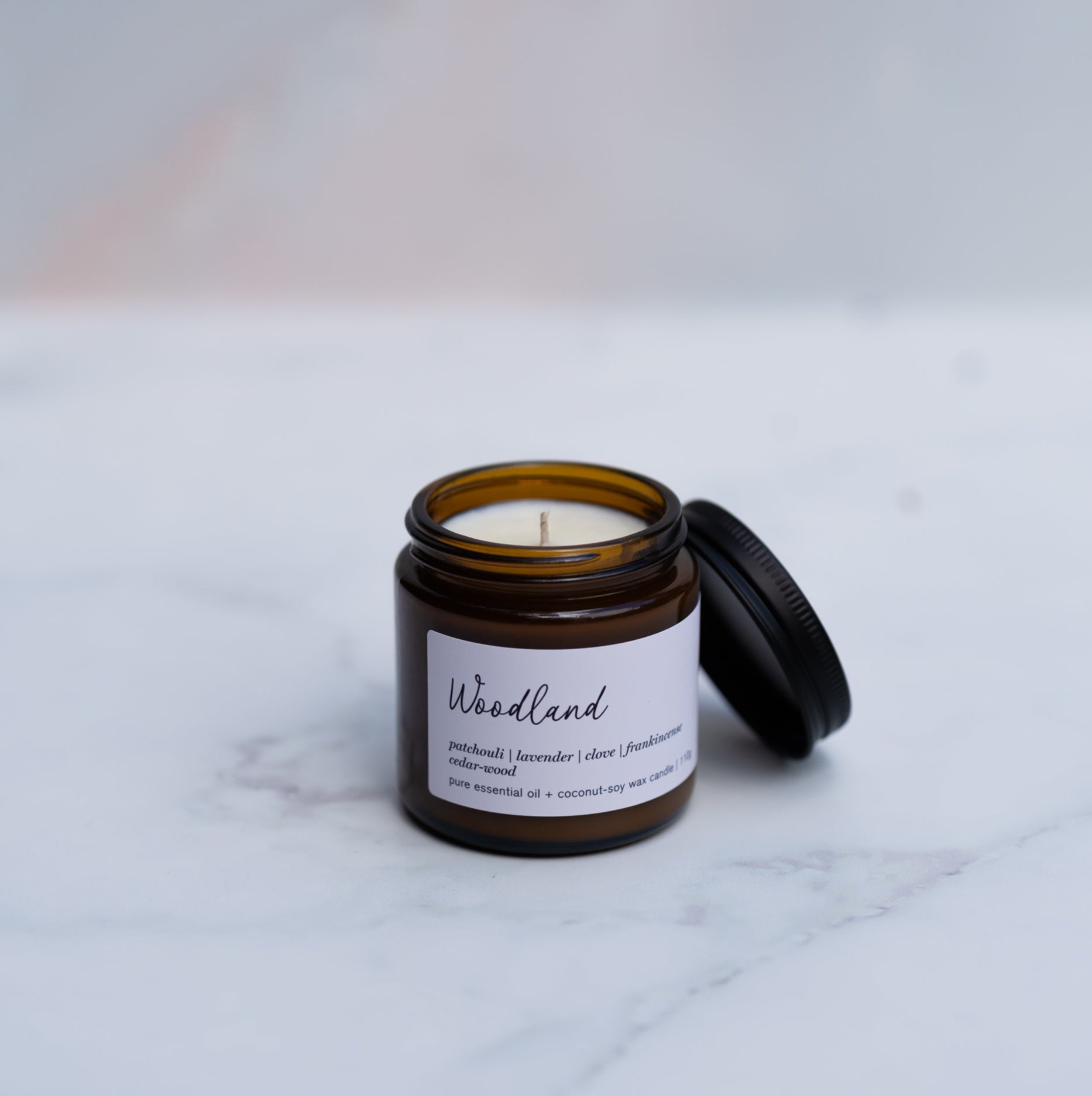Mini Woodland candle in an amber jar with a lid on a marble surface
