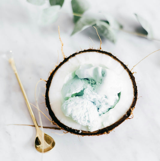 A half coconut shell filled with lime sorbet on a marble surface with a gold spoon and foliage blurred in the background
