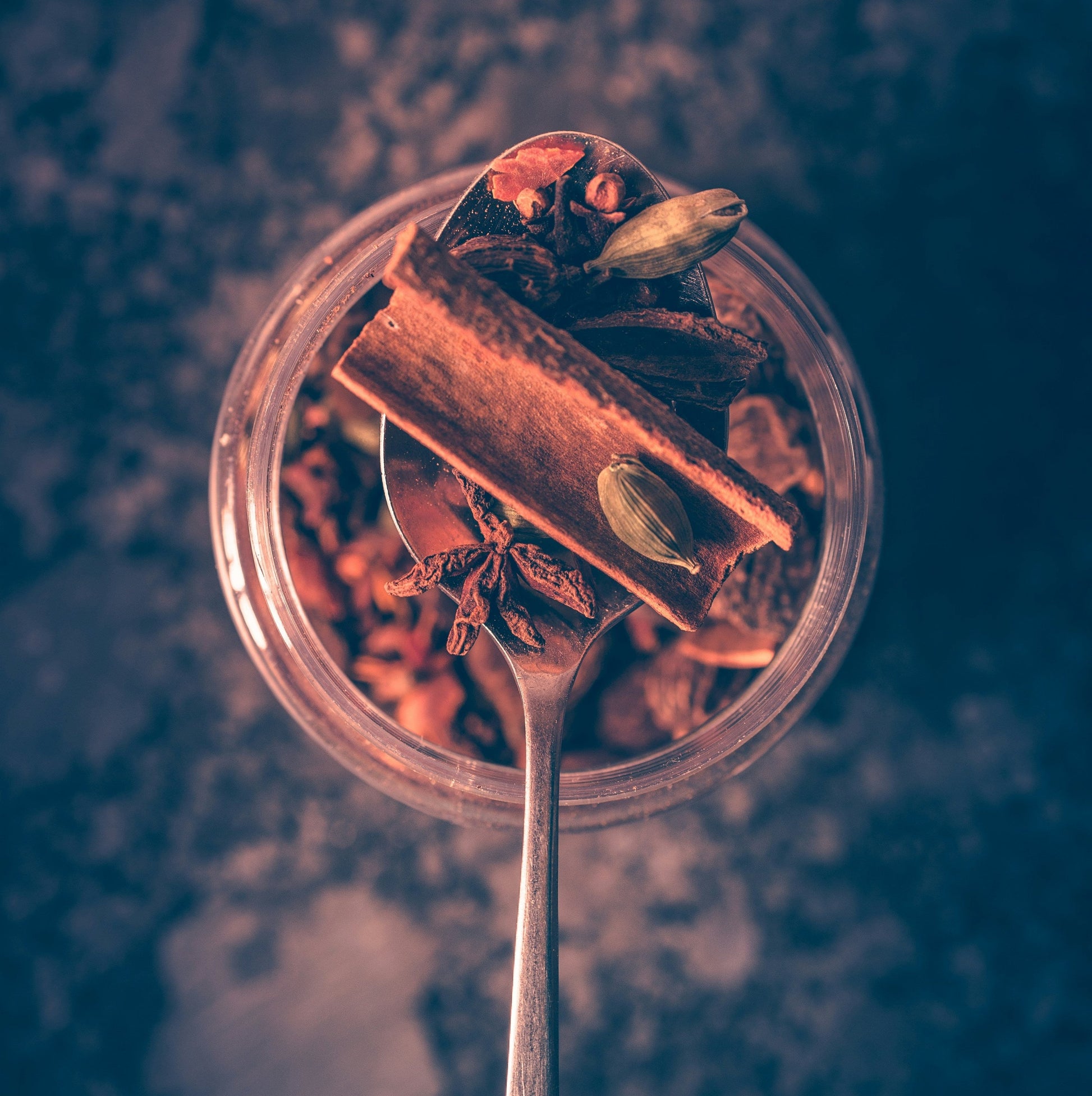 A glass jar with cinnamon, spices, star anise, cardamom pods on a blurred dark background