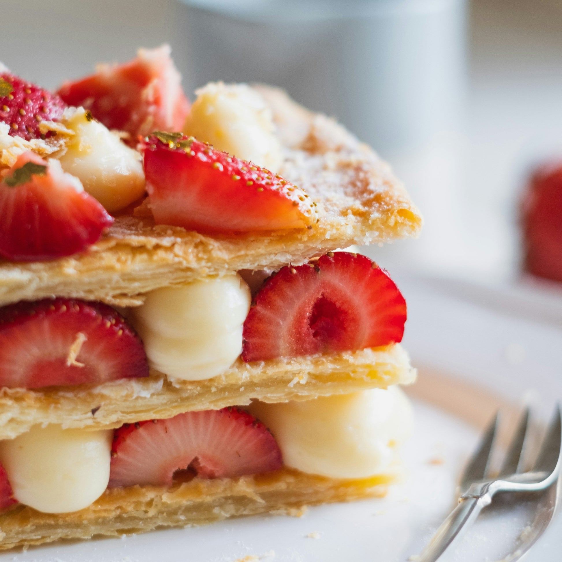 Layered dessert with strawberries and cream on a white surface with a blurred background