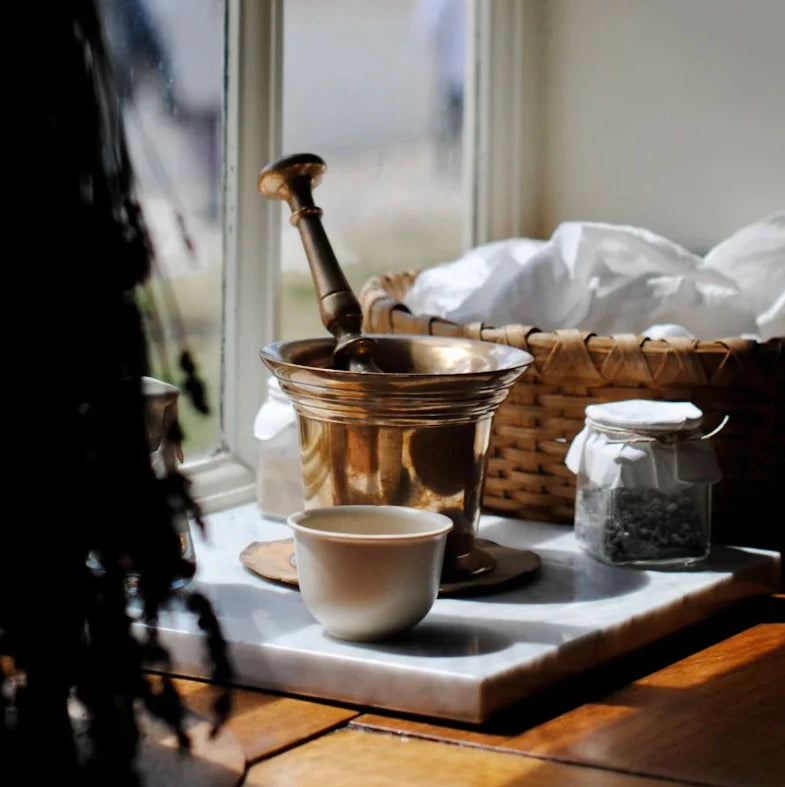 A brass mortar and pestle on a marble board next to a basket and some dried lavender
