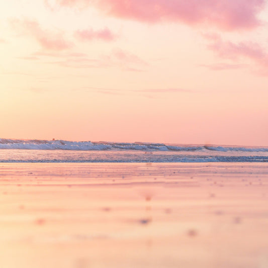 Image of ocean with gentle waves and pink golden sky and peachy vanilla coloured sands.