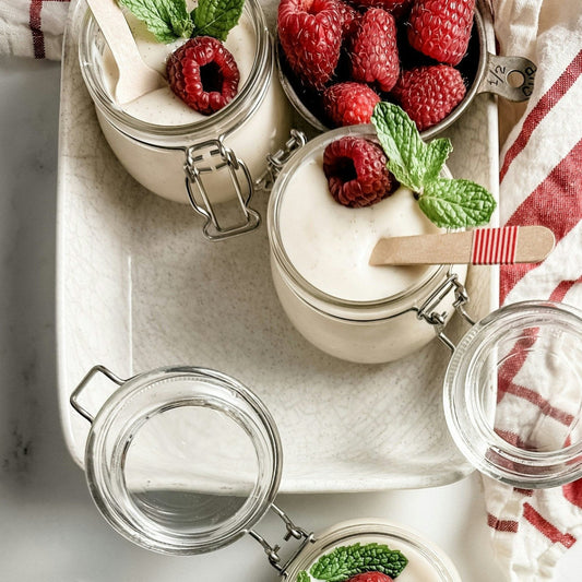 A tray with pots of vanilla pudings topped with raspberries garnished with mint leaves