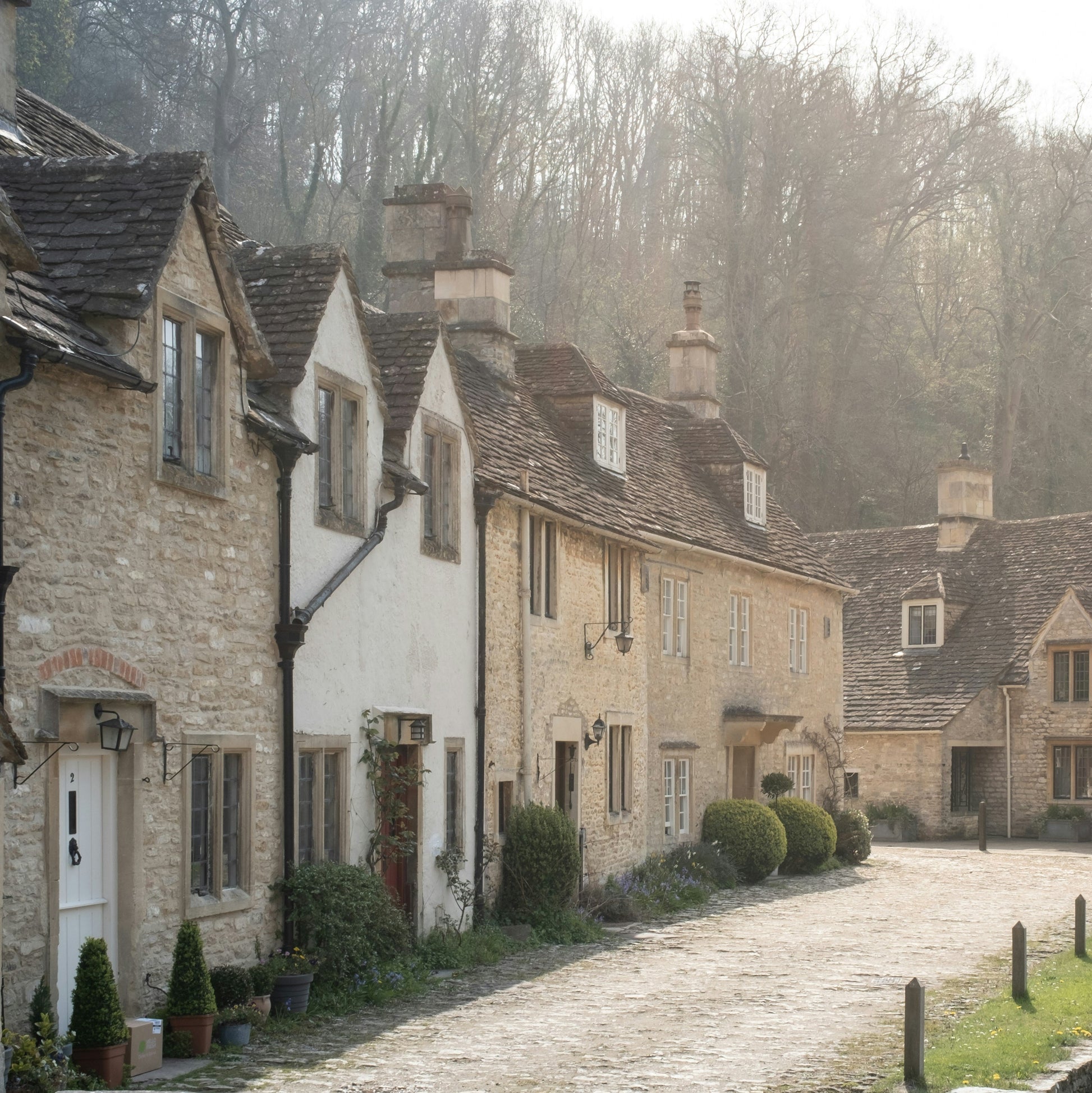 A row of English cottages on a cobblestone street with a wooded forest in the background