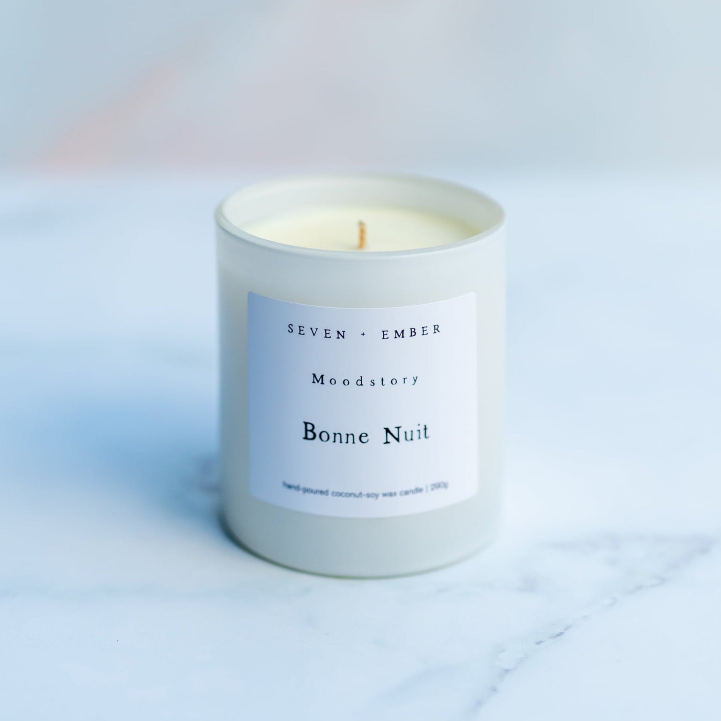 Bonne Nuit moodstory candle in a white glass vessel on a marble background