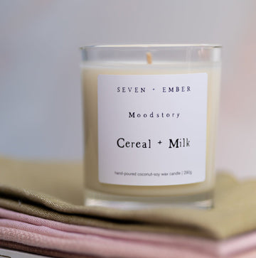 Cereal and milk mood story candle sitting atop a sage green and pink cloth and a book