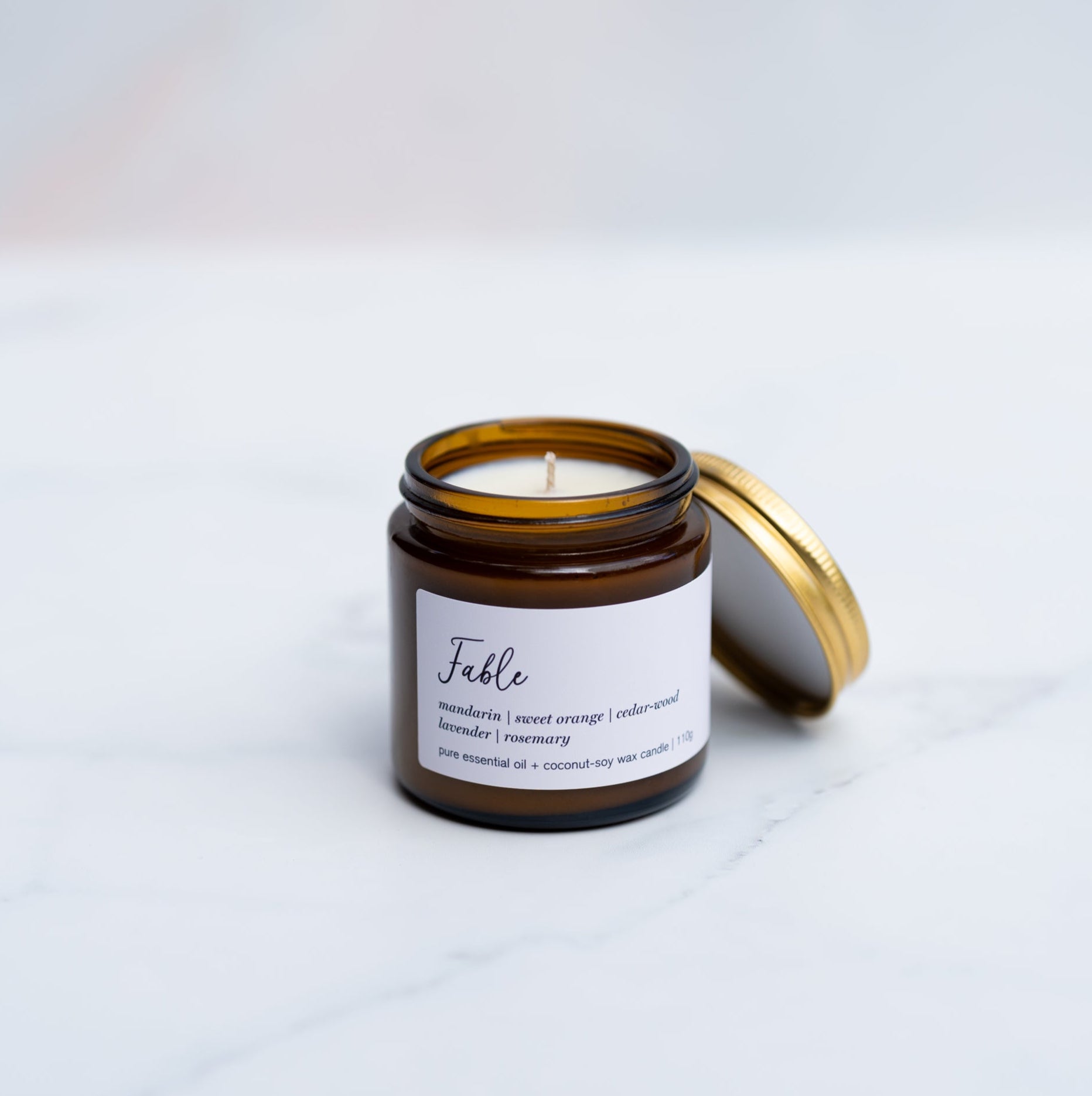 A mini Fable candle in an amber jar with a gold lid sitting atop a marble surface