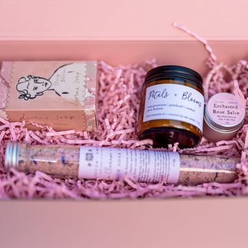A sample of the Seven and Ember monthly candle subscription box with a boxed soap, an enchanted rose salve, a mini Petals and Blooms candle and a bath salt tube