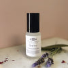 A bottle of Quiescence room spray with lavender sprig on a marble surface with a blured pink background