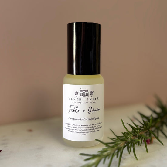 Bottle of fable and grove essential oil room spray mist on a marble surface on a dusky pink background with a sprig of rosemary laying next to the bottle