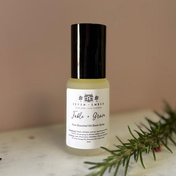 Bottle of fable and grove essential oil room spray mist on a marble surface on a dusky pink background with a sprig of rosemary laying next to the bottle