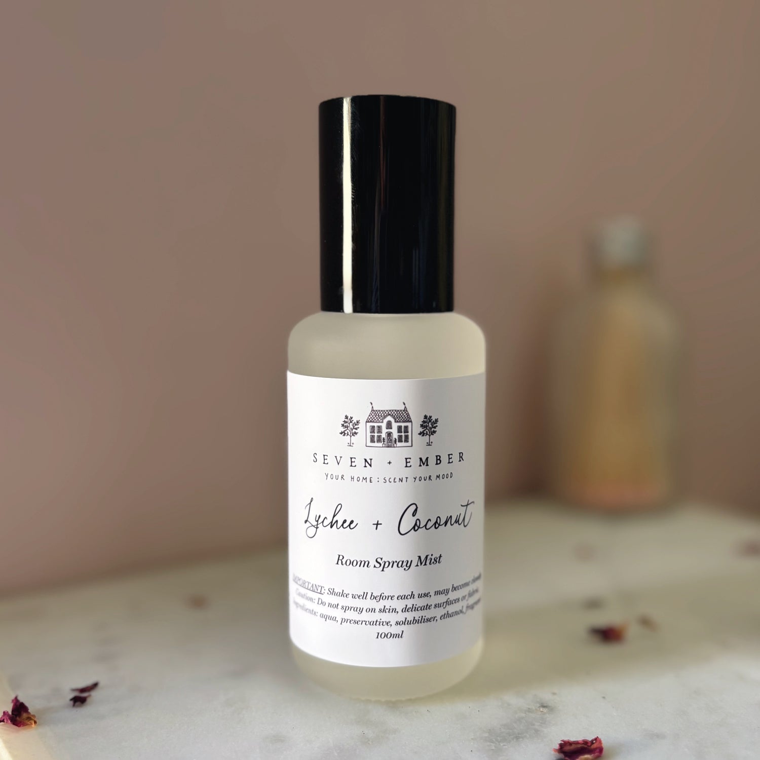 Bottle of lychee and coconut room spray mist on a marble surface with a blurred pink background