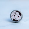 Aluminium tin of lip balm with a screen printed label of a girl with a big hair bow and pink rosey cheeks on a marble background