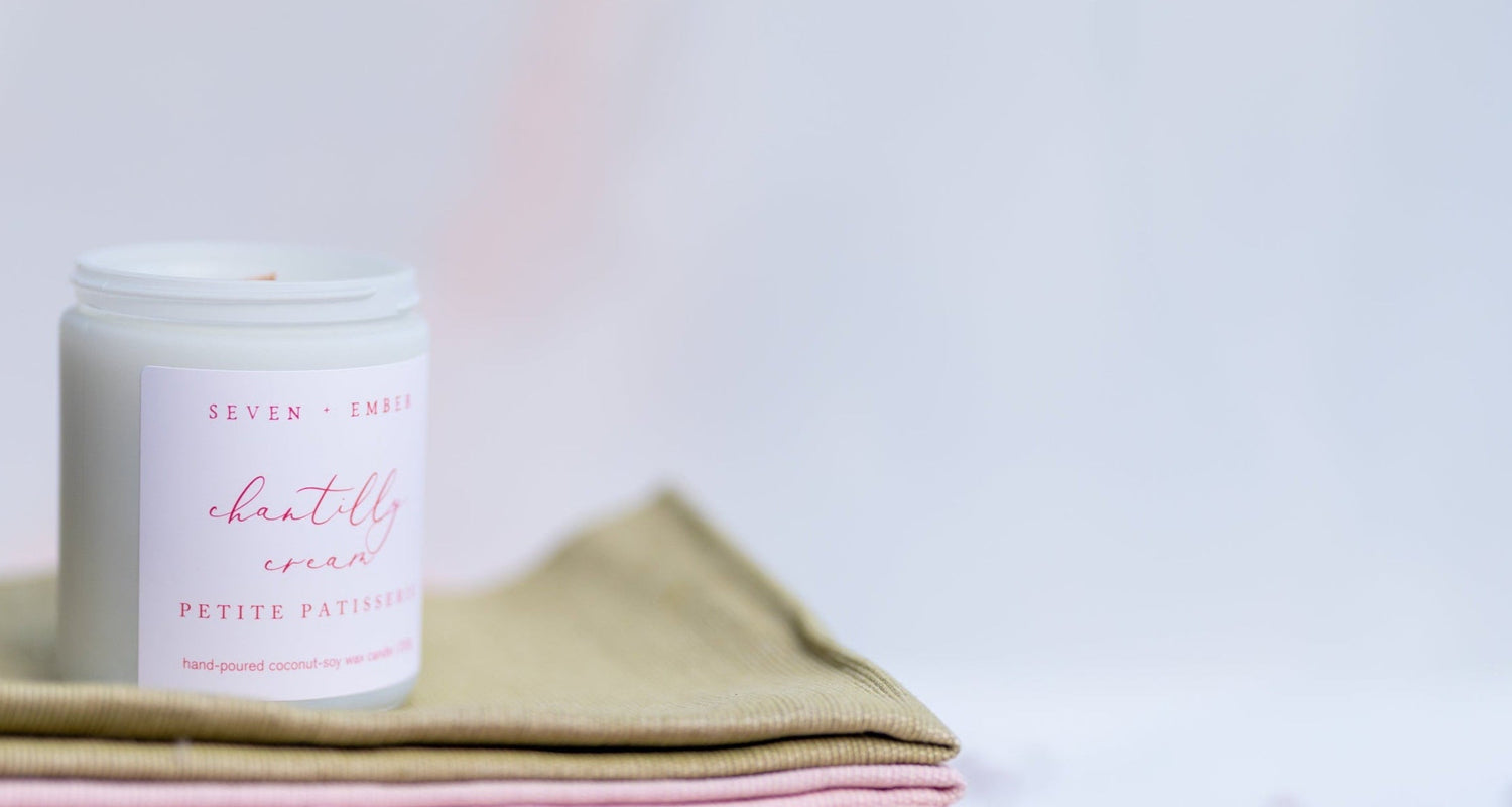 Chantilly cream candle in a white vessel on a green and pink cloth on a white blurred background