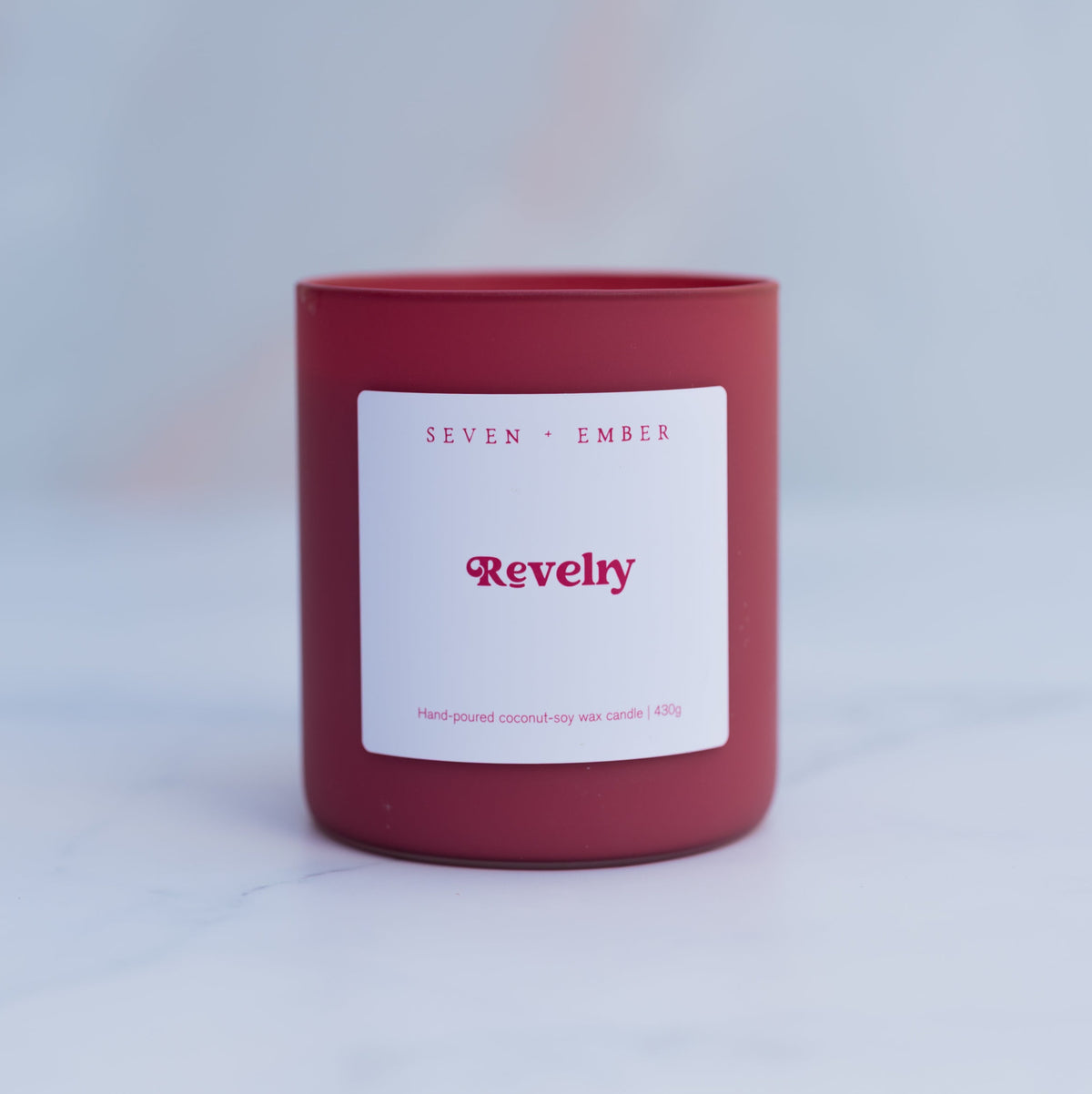Revelry candle in a red frosted glass vessel on a blurred marble background