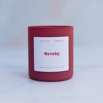 Revelry candle in a red frosted glass vessel on a blurred marble background