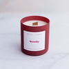 Revelry candle with a wooden wick in a red coloured frosted vessel on a blurred marble background