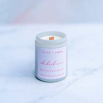 Rhubarb noir candle with a wooden wick in a white screw top jar on a marble surface