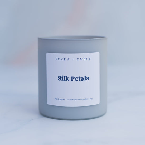 Silk petals candle in a light grey frosted vessel on a blurred marble background