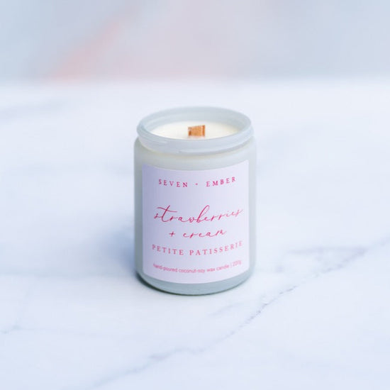 Strawberries and cream candle with wooden wick in a white screw top jar on a marble surface