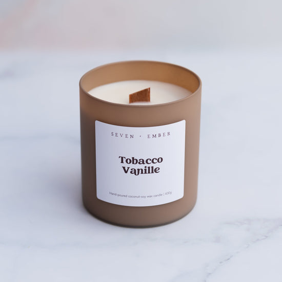 Tobacco vanilla candle with wooden wick in a coffee coloured frosted glass vessel on a blurred marble background