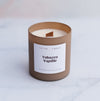 Tobacco vanilla candle with wooden wick in a coffee coloured frosted glass vessel on a blurred marble background