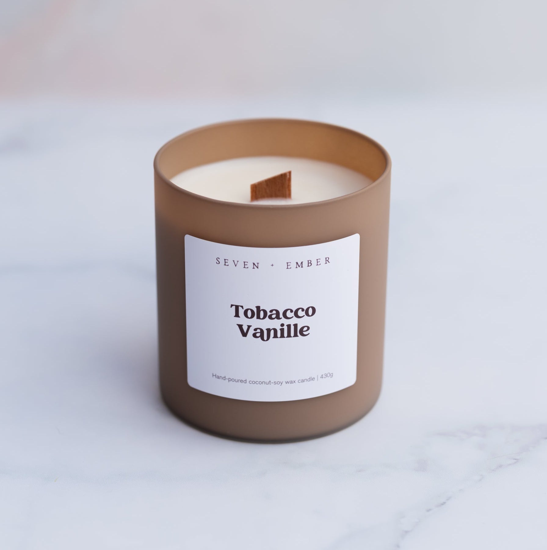 Tobacco vanilla candle with wooden wick in a coffee coloured frosted glass vessel on a blurred marble background