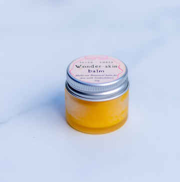 Wonder skin balm in a mini frosted jar with silver lip filled with sunshine yellow balm on a marble surface