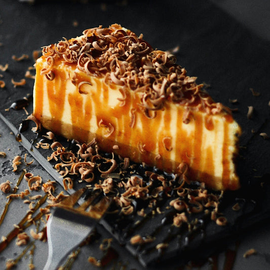 A slice of caramel cake with caramel sauce and grated chocolate on a black plate with a small fork