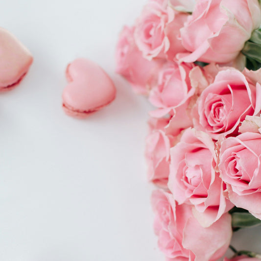 A bunch of pretty pink roses and two love heart shaped pink macarons on a white background