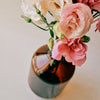 A bouquet of pink wild roses in a amber coloured bottle vase on a creamy background