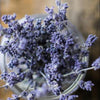 A bunch of lavender blooms in a glass jar sitting atop a timber background