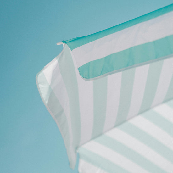 A aquamarine and white striped beach umbrella up against a backdrop of bright blue sky