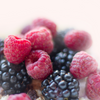 A pile of berries, raspberries and blackberries on some whipped cream