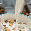 A bowl of cereal in a white bowl with a teal rim with milk being poured in