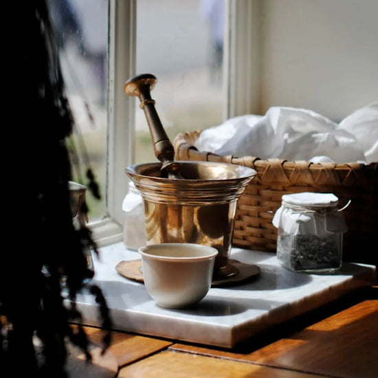 A brass mortar and pestle on a marble board next to a basket and some dried lavender