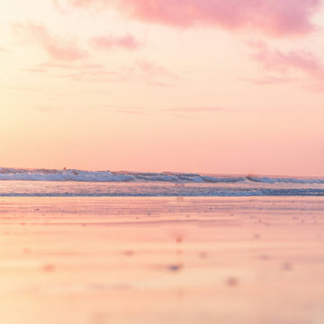 Image of ocean with gentle waves and pink golden sky and peachy vanilla coloured sands. 