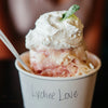 A cup of Lychee sorbet labeled lychee love topped with a swirl of whipped cream and a mint leaf on a blurred background