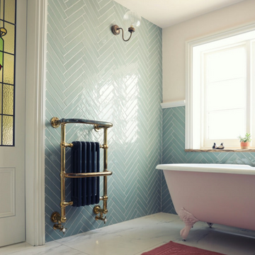 Pink bathtub in a bathroom with sage green herringbone wall tiles and a white marble floor 